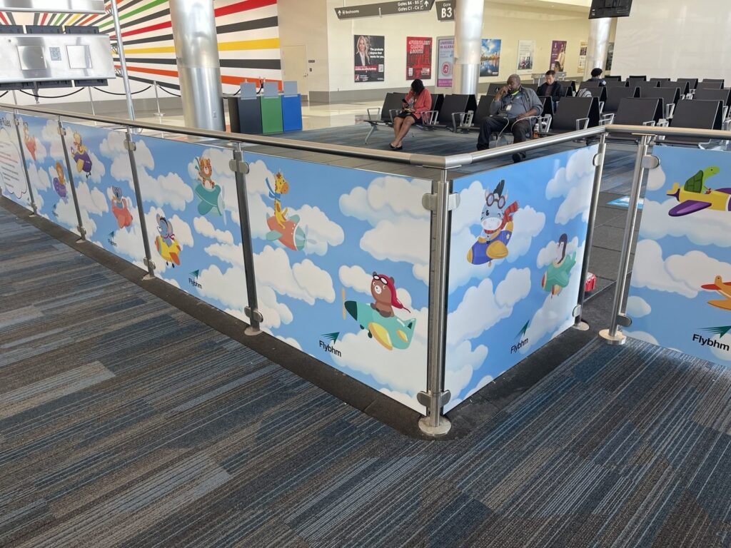 Angled view showing adjoining sections of Birmingham airport Kids Zone graphics on two sides of the railing enclosure.