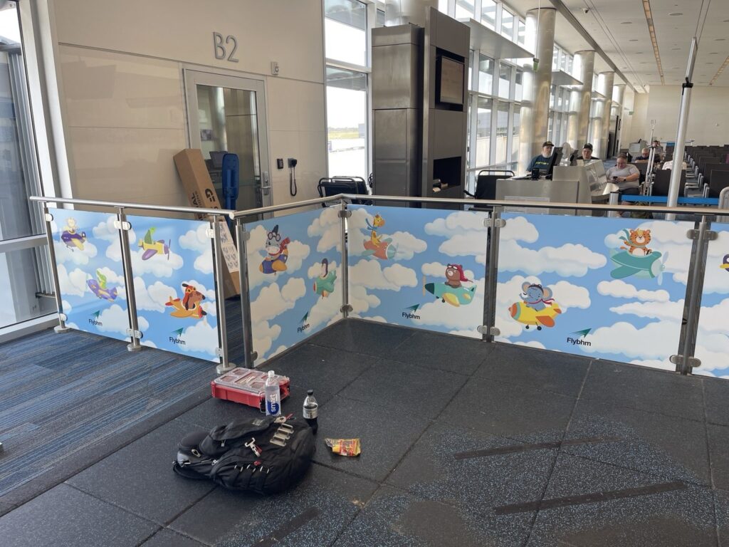 Corner view of Birmingham airport children's play area railing panels decorated with cartoon animals flying airplanes against blue sky and clouds.