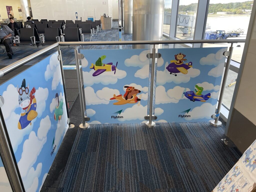 Close view of airport railing panels with cartoon zebra, turtle, monkey and other animal pilots in colorful airplanes, plus FlyBHM marks.