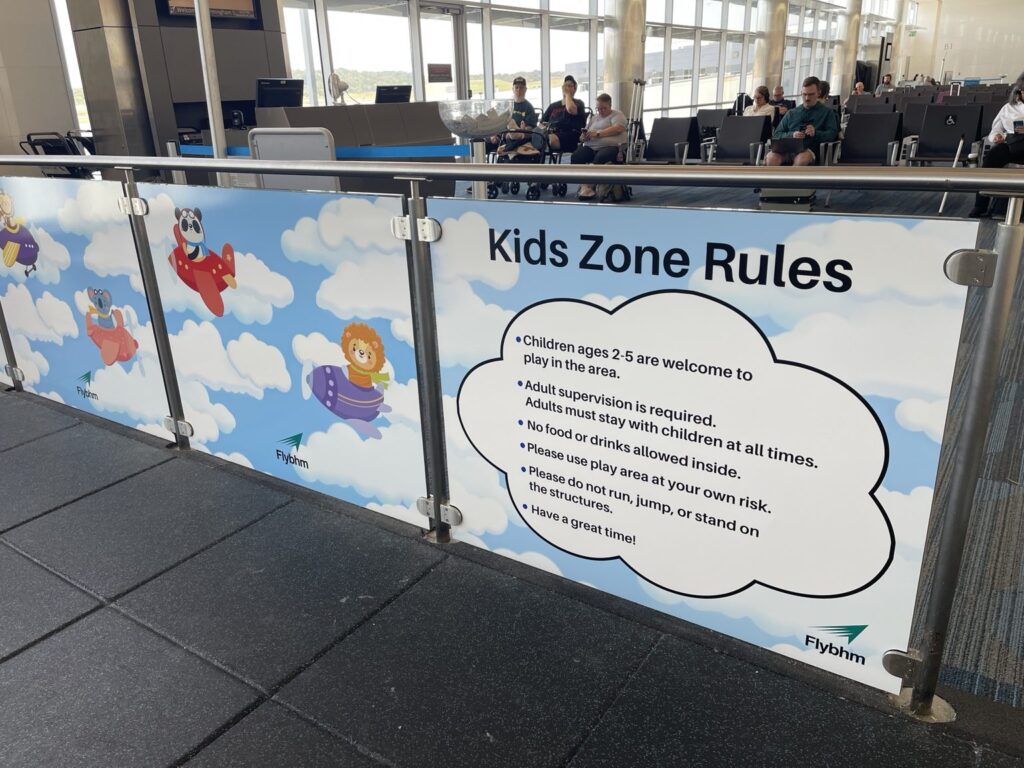 Close view of Kids Zone Rules text within a cloud-shaped graphic attached to a metal railing at Birmingham airport.