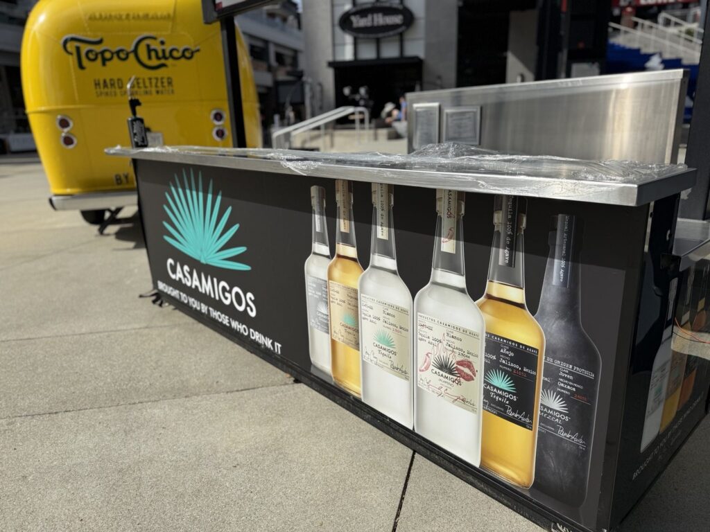 Close side view of Casamigos counter graphics with agave logo and illustrated tequila bottles, with a yellow vehicle in the background.
