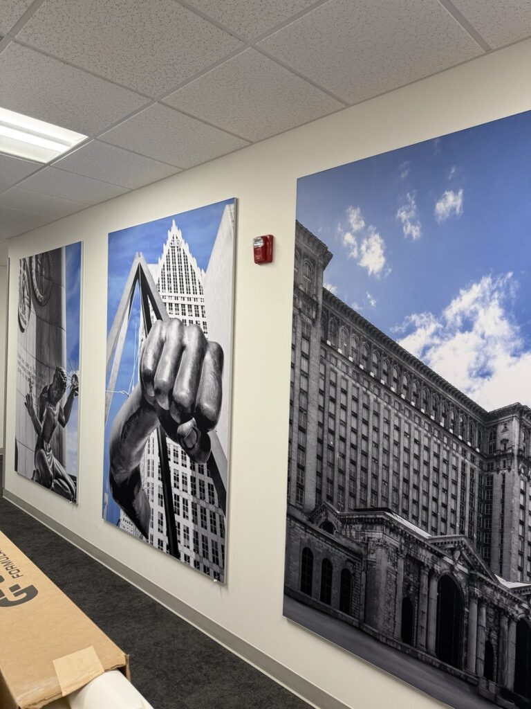 Angled view of large mounted Detroit architectural photo panels with selective blue skies in a medical building hallway.