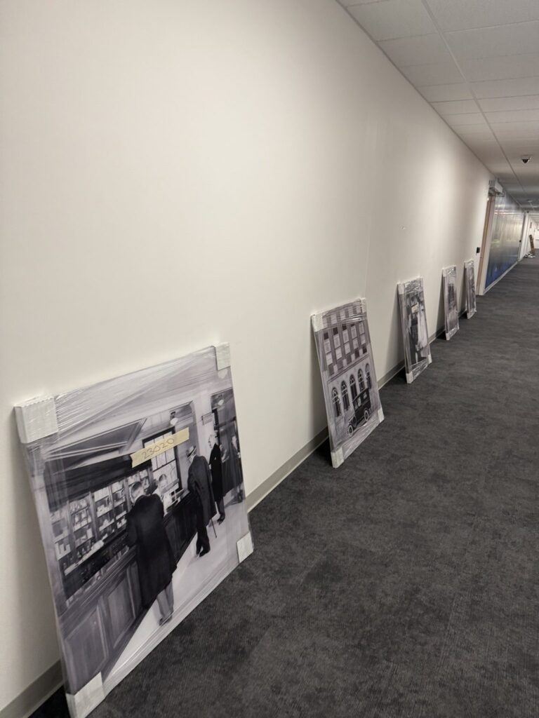 Black-and-white printed photo panels wrapped and leaning along the wall of a long carpeted hallway before installation.