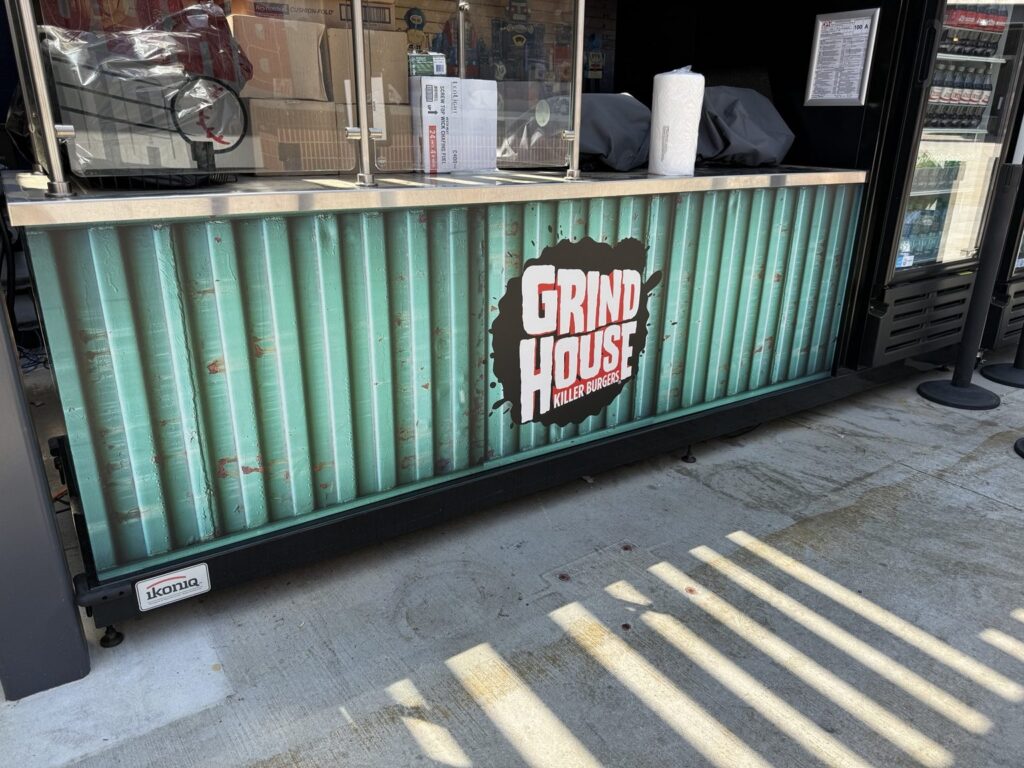 Wide view of Grindhouse Killer Burgers concession counter wrap with bold white and red logo on textured teal industrial-style print.