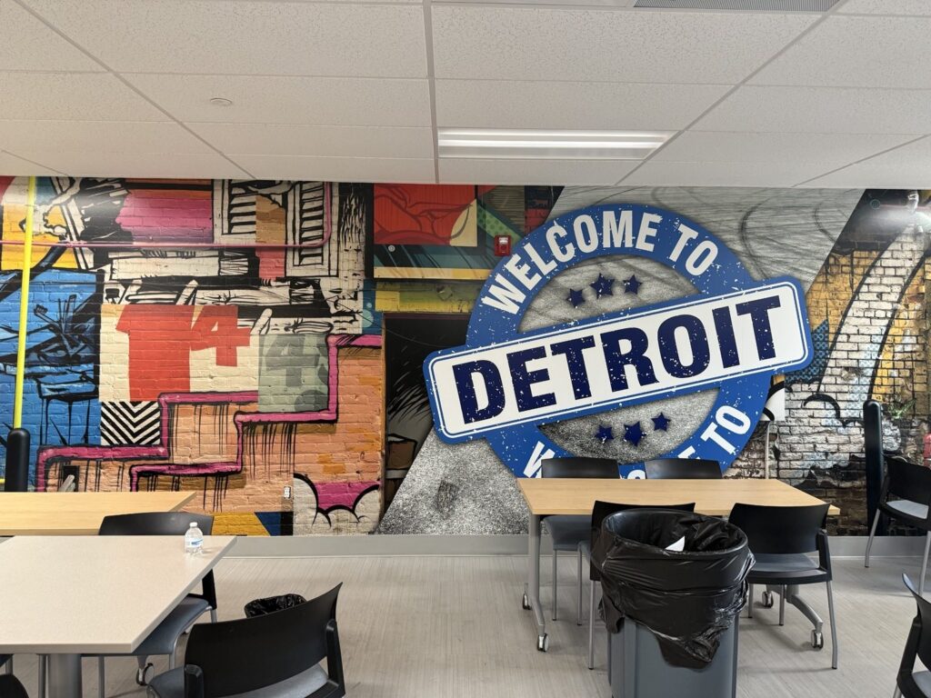 Close-up of bright Detroit wall mural with a large blue and white WELCOME TO DETROIT circular emblem and multicolored street art graphics.