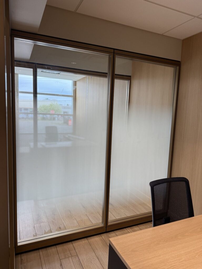 View from inside a private glass-walled dealership office showing a white frosted gradient across two partition panes beside a desk chair.