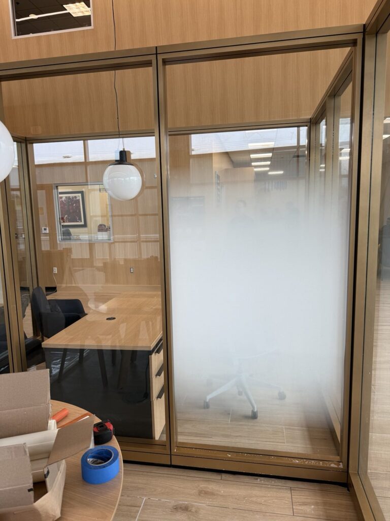Close view of bronze-framed glass office at a Kia dealership showing soft white frosted gradient privacy film across the interior partition.