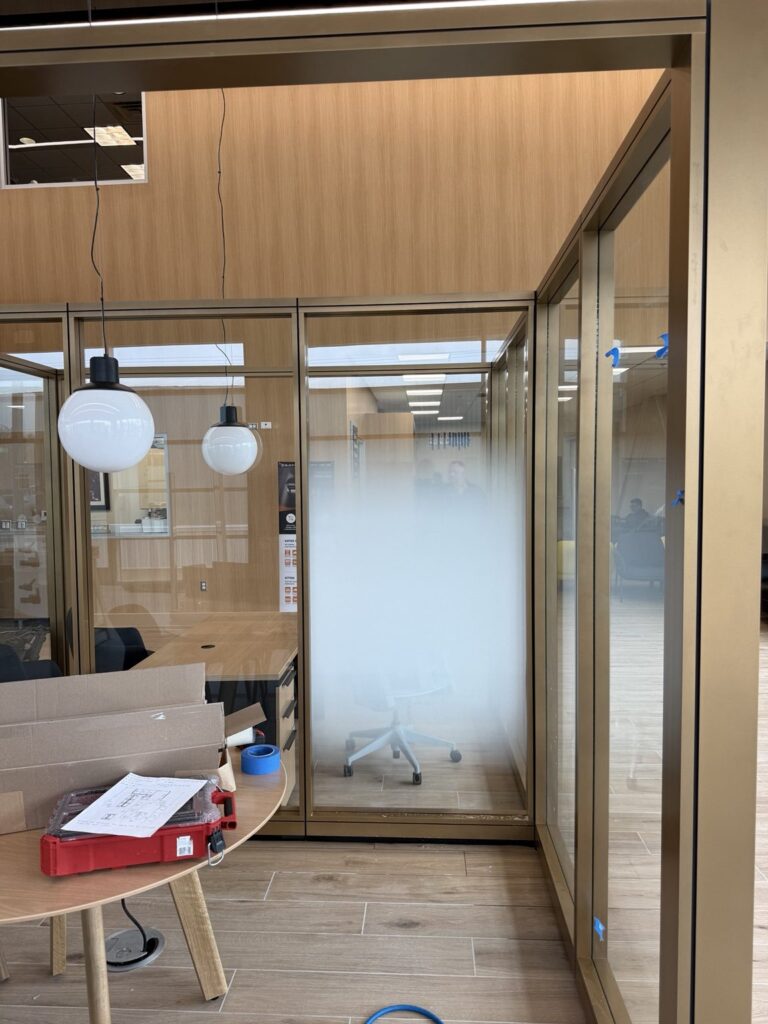 Glass-walled dealership office with frosted gradient privacy film, round pendant lights and red tool case in foreground.