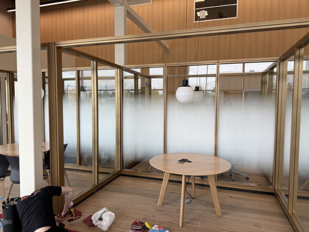 Wide interior view of glass-walled dealership offices featuring white frosted privacy gradients, pendant lights and installation work area.