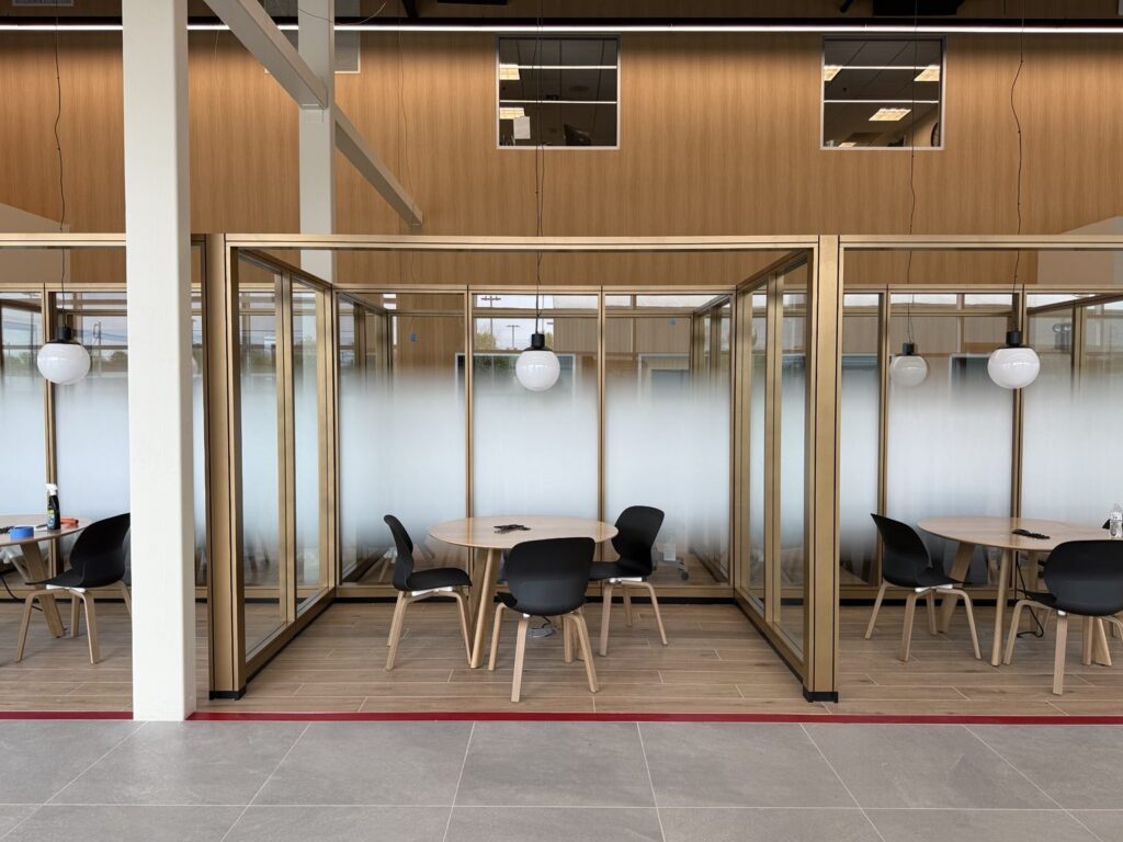 Straight-on view of bronze-framed dealership office partitions with horizontal frosted gradient film and round meeting tables.