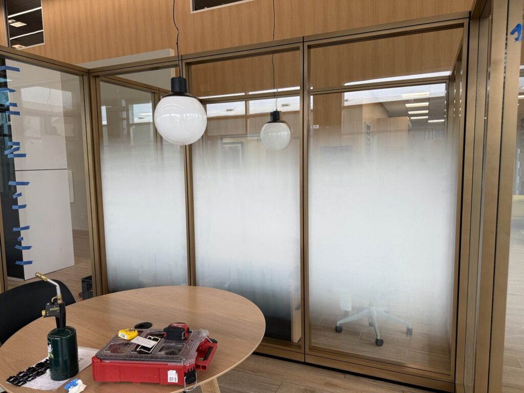 Two adjoining dealership glass office partitions with matching frosted gradient film and a worktable with installation tools in front.
