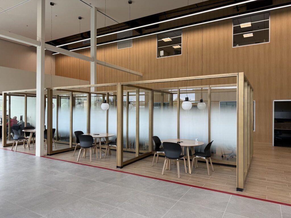 Wide view of a Kia dealership interior with bronze-framed glass meeting areas and coordinated white frosted gradient privacy film.
