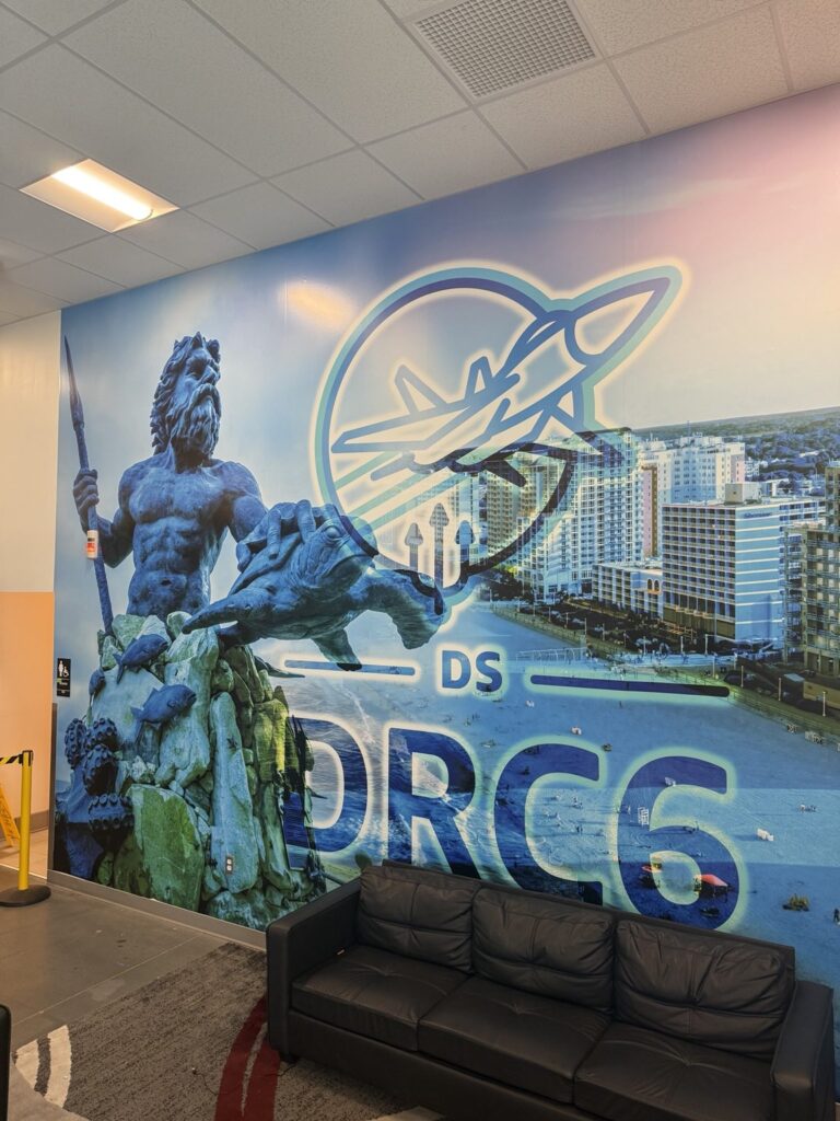 Angled close view of large wall wrap combining King Neptune statue, Virginia Beach buildings, oceanfront and DRC6 aviation graphic.
