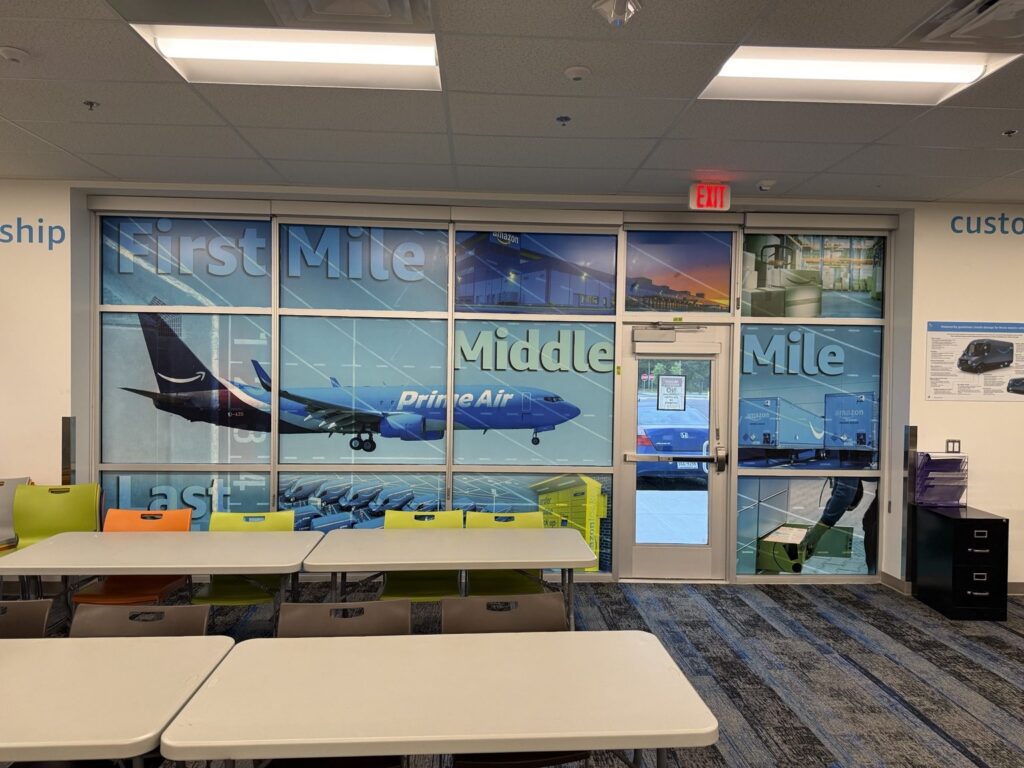 Interior glass wall and door covered with Amazon logistics graphics featuring a Prime Air airplane and First Mile, Middle Mile and Last Mile messaging.