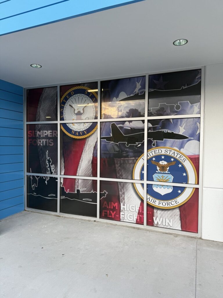 Close view of military-themed window graphic with United States Navy and Air Force seals, aircraft silhouettes and flag background.