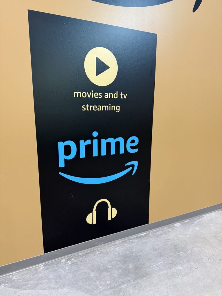 Close-up of black Amazon Prime wall panel with blue Prime wordmark, streaming play symbol, and headphone graphic.