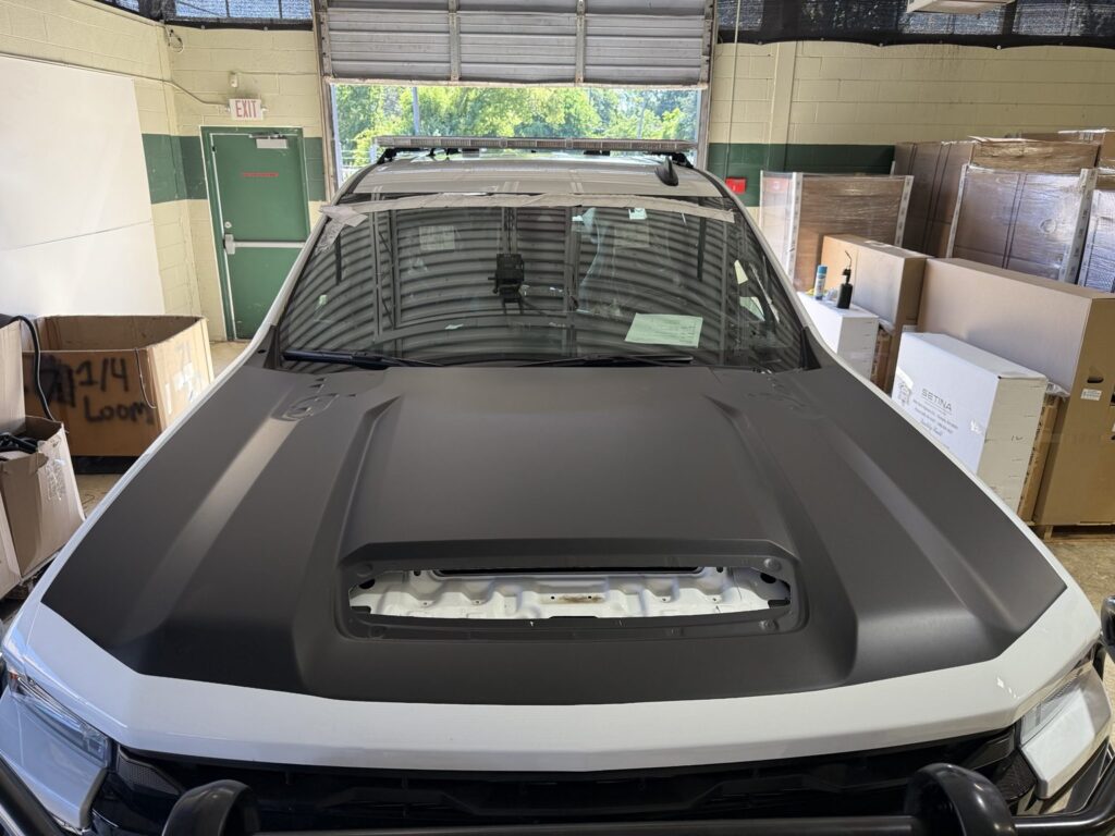 Front view of white Chevrolet Alaska State Troopers pickup with a black hood and roof lightbar in a workshop