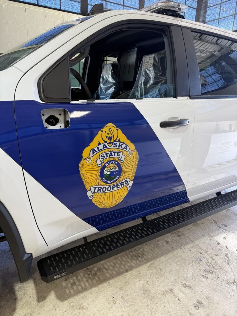 Close-up of blue Alaska State Troopers door graphic with large gold badge on a white heavy-duty Chevrolet pickup