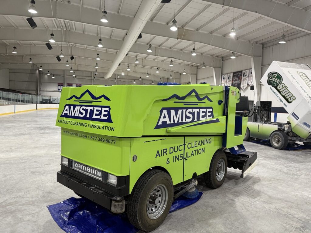 Three-quarter view of Amistee-branded Zamboni with fluorescent green panels and navy logos in Flint, Michigan