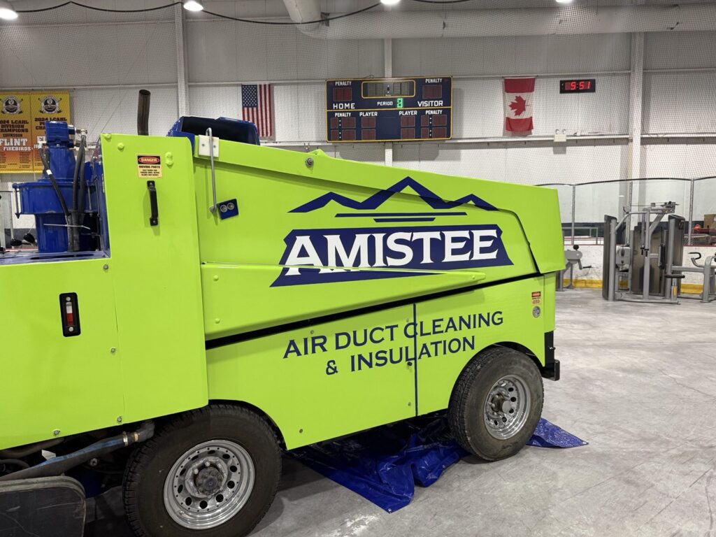 Amistee Zamboni with lime-green and navy graphics inside a Flint, Michigan hockey arena near the scoreboard