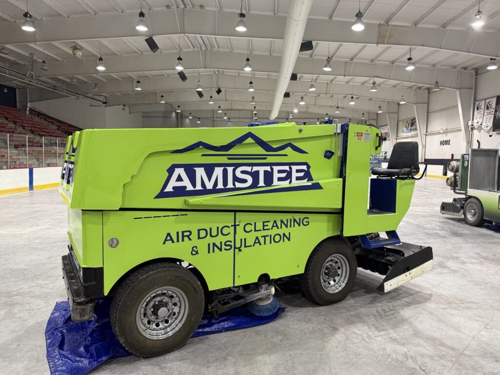Side view of Amistee lime-green Zamboni with navy logo, air duct cleaning and insulation graphics, and operator seat