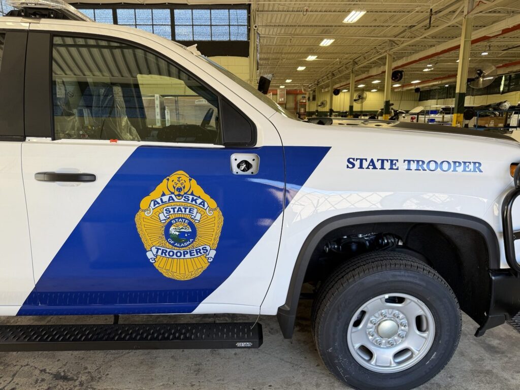 Law enforcement fleet graphics: white Chevrolet 2500HD with blue Alaska State Troopers door stripe, gold badge and STATE TROOPER lettering