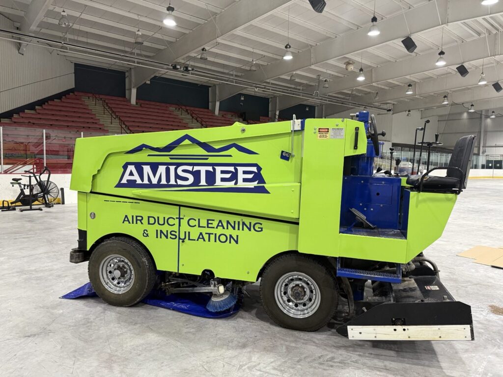 Zamboni wrap installation: side profile of lime-green Amistee Zamboni with navy logo and air duct cleaning and insulation graphics